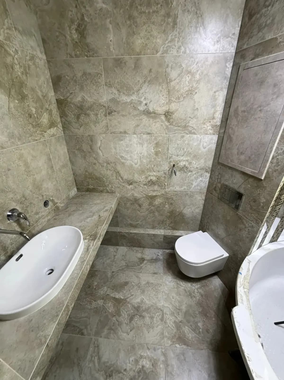 Graues Bad mit Mosaik, Wanne und integrierter Ablage Ansicht 2